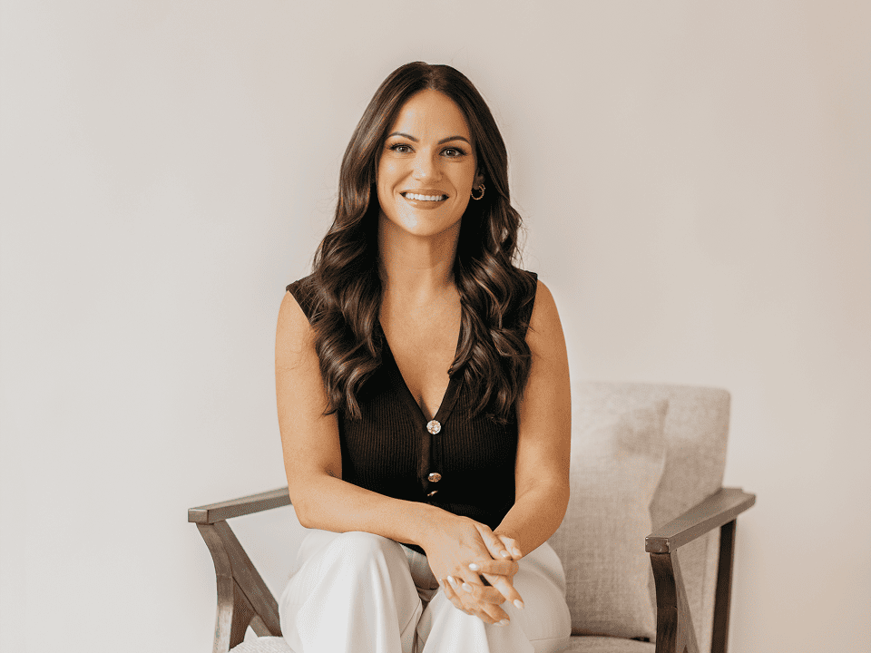 Ashley Sweet sitting casually in modern office setting, wearing black blazer